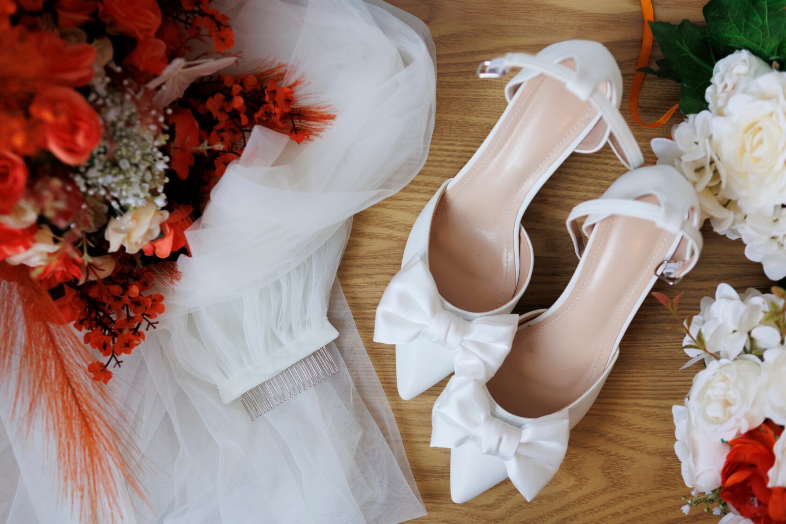 White bridal shoes arranged beside vivid orange flowers