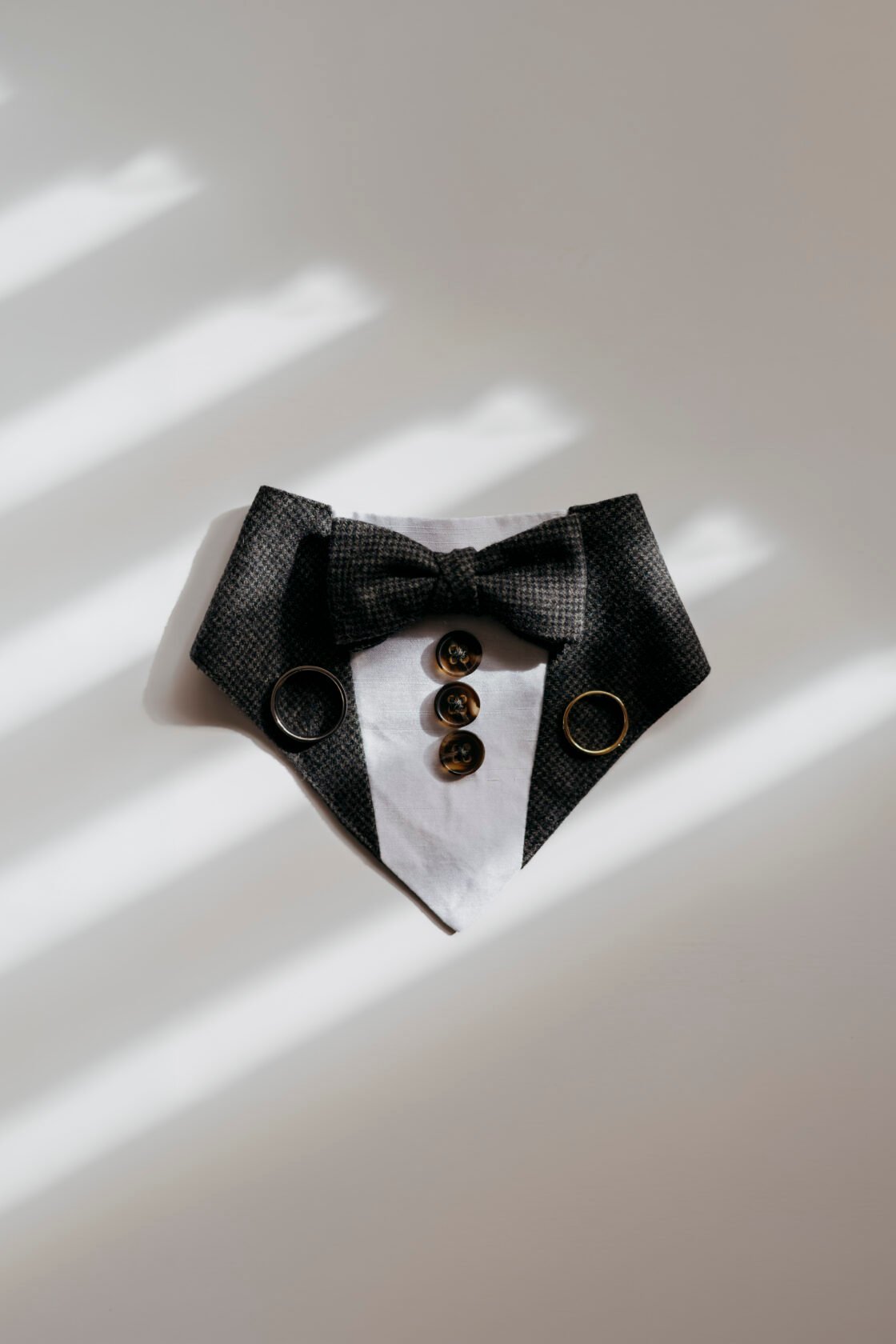 Groom bow tie, buttons and wedding rings arranged in window light