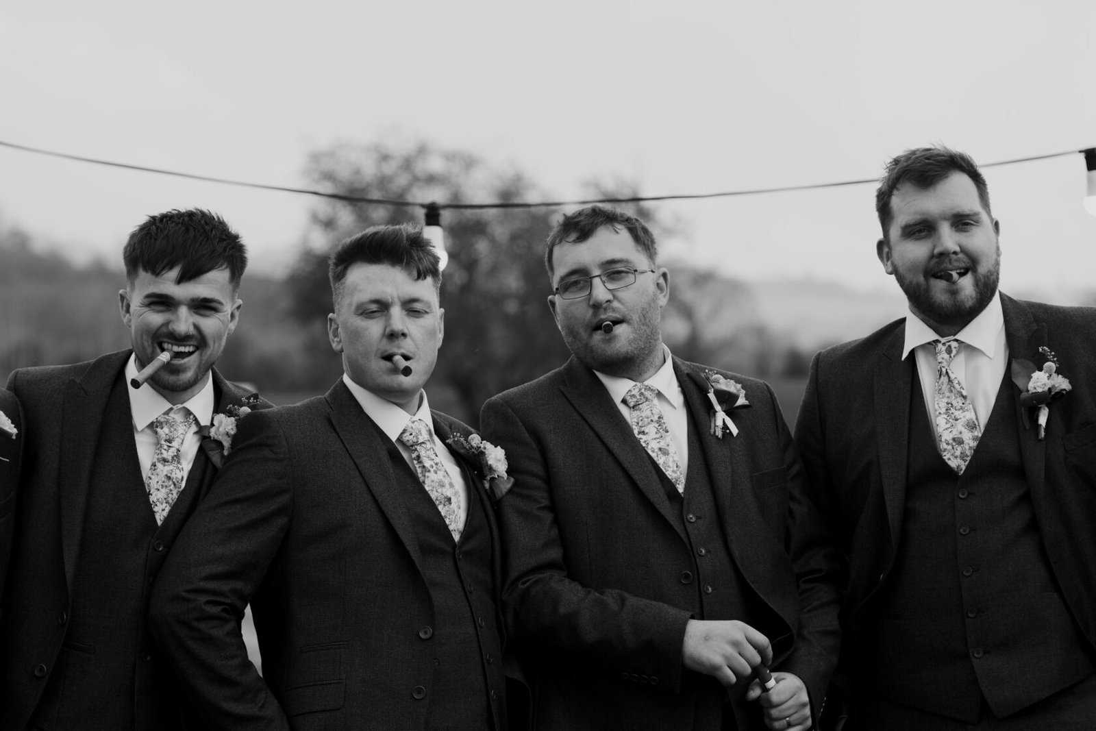 Groomsmen sharing cigars together in black and white