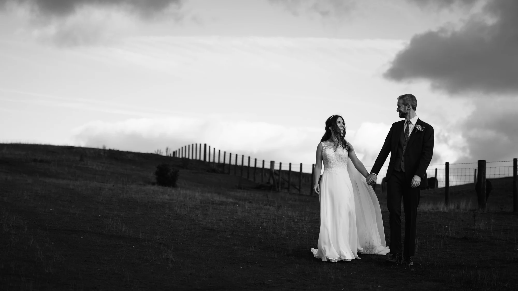 Amy and James holding hands beneath an open sky in a black-and-white countryside portrait