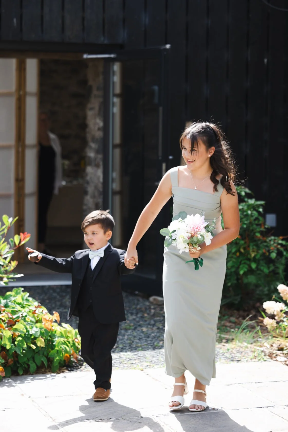 Young page boy walking hand in hand with a bouquet-carrying wedding guest