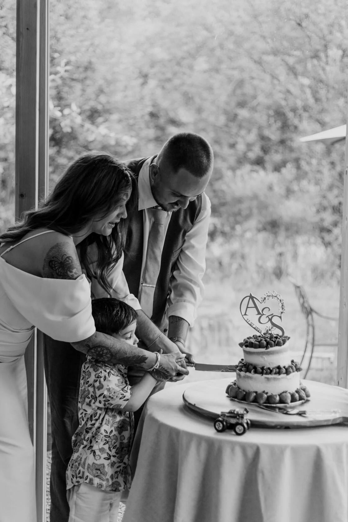 A couple and child cutting a strawberry-decorated wedding cake together