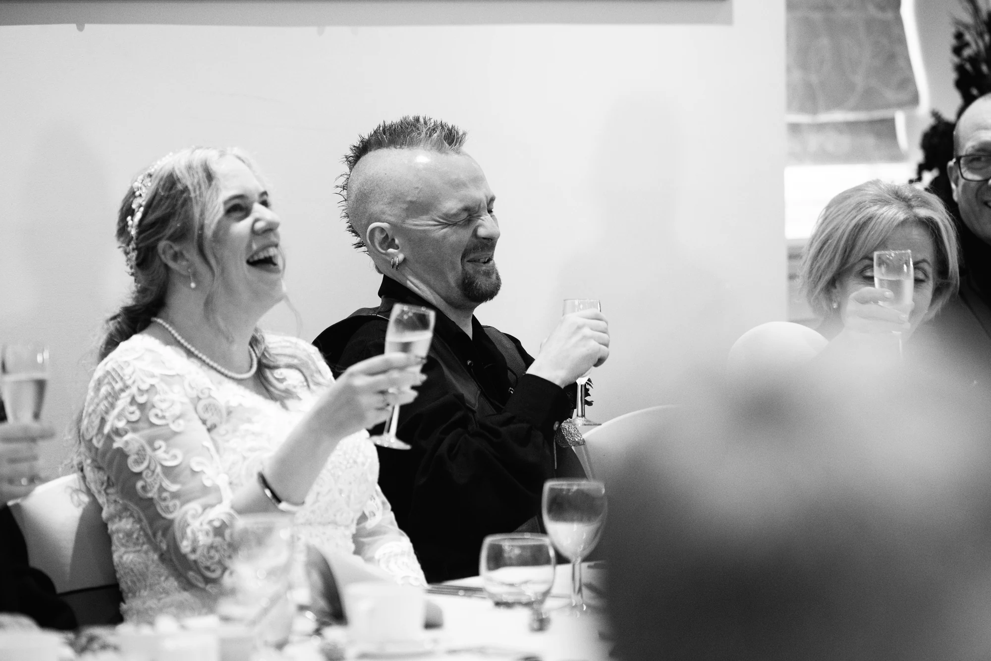 Ruth and David laughing with glasses raised at their wedding reception