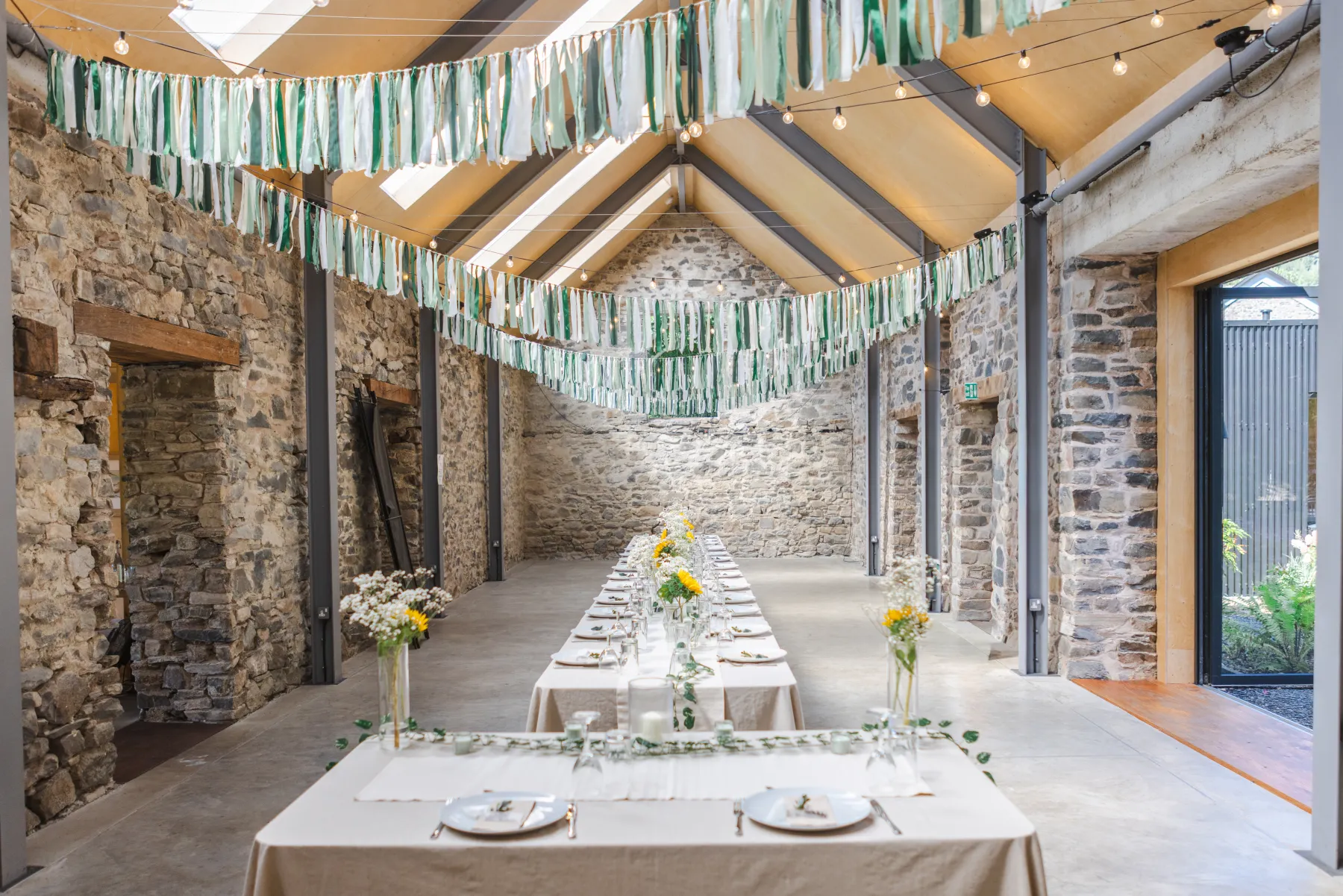 Long wedding tables and green ribbon decorations inside the stone reception barn at Nant y Walch