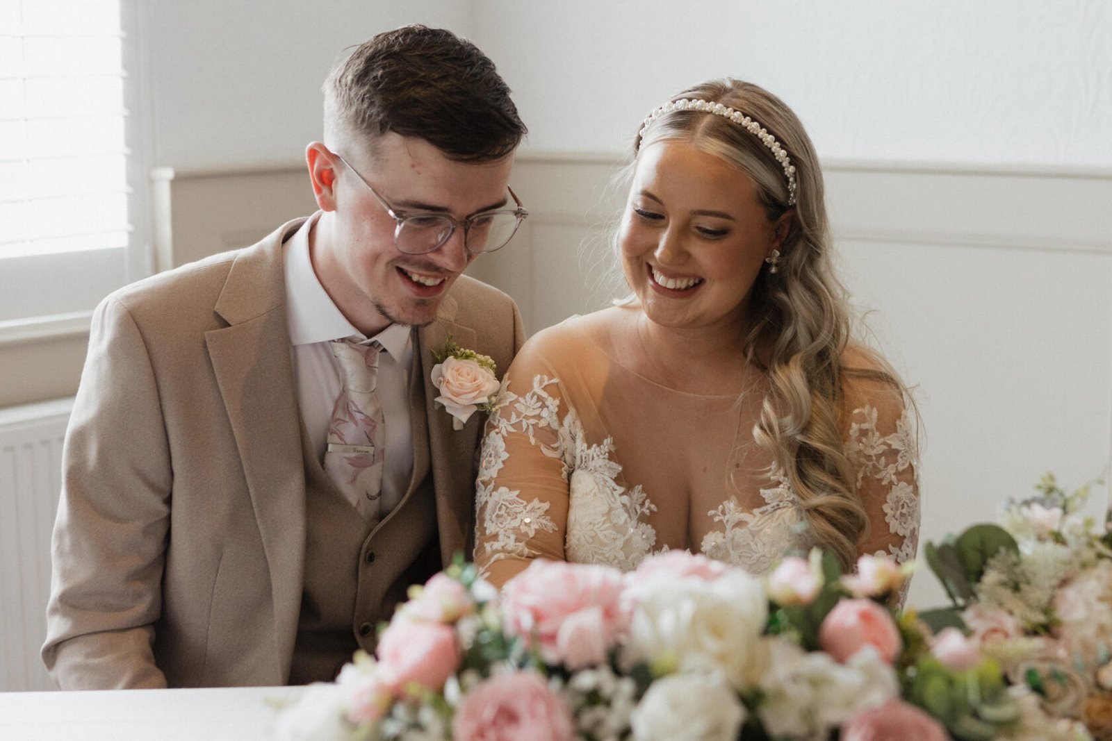Newlyweds smiling together behind soft pink wedding flowers