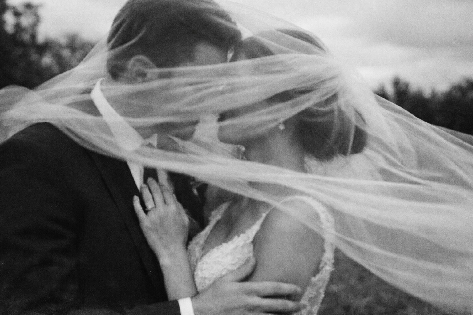 Newlyweds kissing beneath their veil in black and white