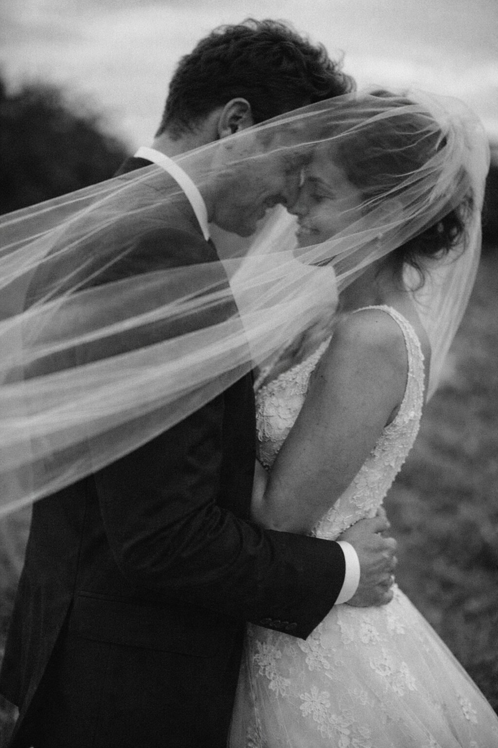 Newlyweds embracing beneath a windswept veil