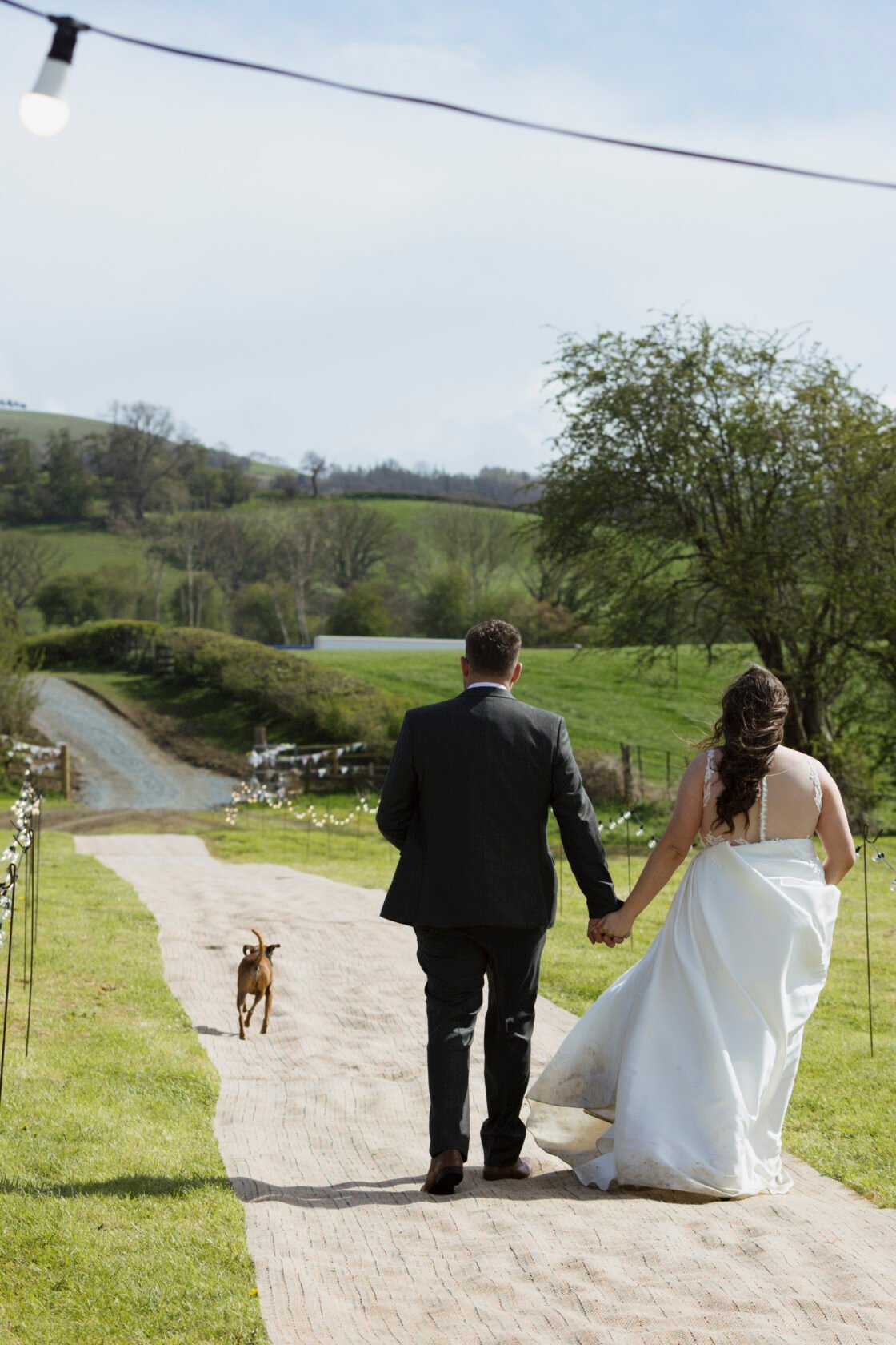 Newlyweds walking hand in hand through their rural wedding reception