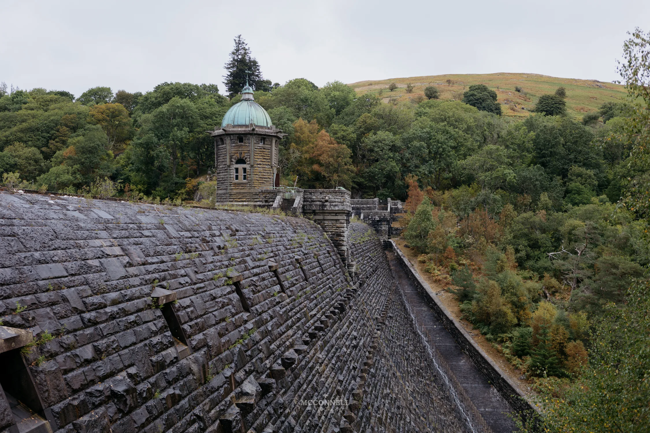 The stone wall and tower of Pen y Garreg Dam surrounded by woodland in the Elan Valley