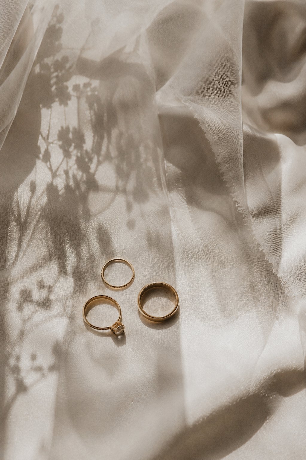 Wedding rings arranged on lace beneath soft floral shadows